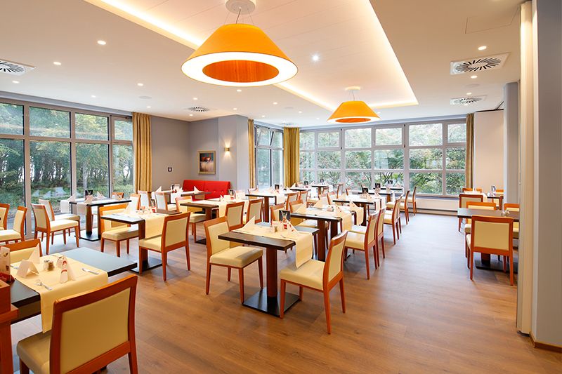 Innenansicht eines stilvollen Restaurants. Helles, modernes Restaurant mit Holzboden, großen Fenstern und orangefarbenen Hängelampen.